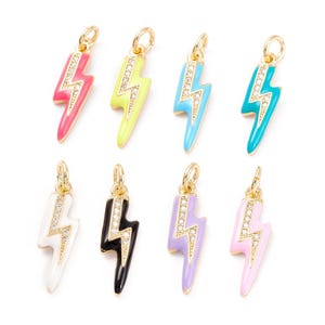 Könnte beinhalten: Sortiment aus zehn Blitzscharms mit goldenen Akzenten und Emaille in verschiedenen Farben, darunter Pink, Gelb, Blau, Türkis, Schwarz, Weiß, Lavendel und Hellrosa. Jeder Charm ist mit einem klaren Strassstein-Design verziert.