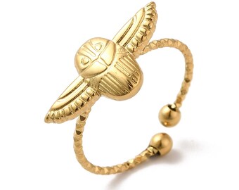 Può includere: Un anello regolabile color oro con un design dettagliato di uno scarabeo con le ali. L'anello ha una fascia testurizzata.