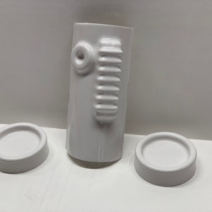 May include: Three white ceramic pieces, one tall and cylindrical with a textured design, and two smaller round pieces.