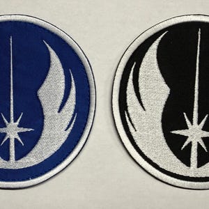 Puede incluir: Dos parches bordados circulares. Uno es azul con un emblema plateado de una línea vertical sobre una estrella y alas. El otro es negro con un emblema plateado.