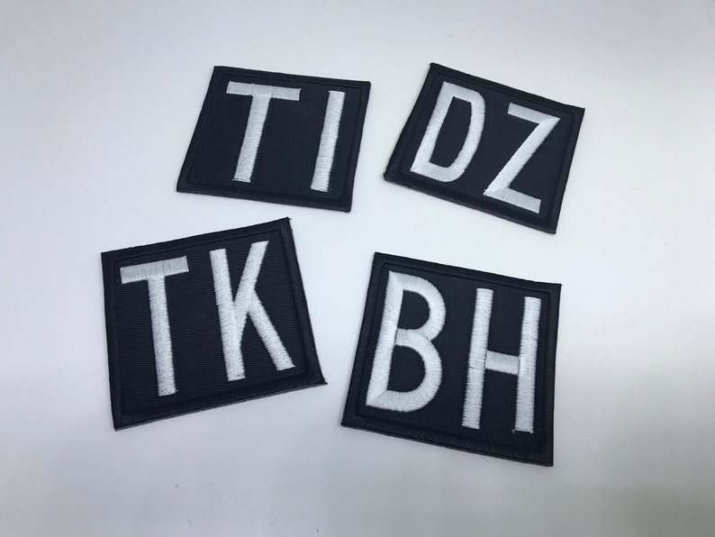 May include: Four black fabric patches with white embroidered letters. The patches spell out "T I D Z" and "T K B H".