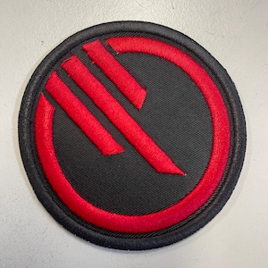 May include: A black and red embroidered patch with a stylised symbol of three vertical lines inside a circle.