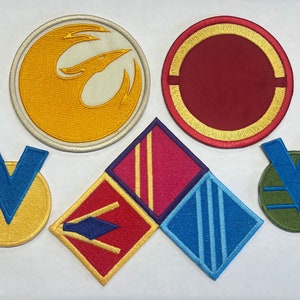 Può includere: Cinque toppe ricamate con diversi disegni. Le toppe sono gialle, rosse, blu, verdi e viola. Le toppe sono tutte di forme e dimensioni diverse.