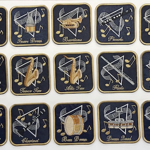 May include: A collection of embroidered patches featuring various musical instruments, including a sousaphone, snare drum, baritone, piccolo, and battery. Each patch has a navy blue background with gold accents and musical notes.
