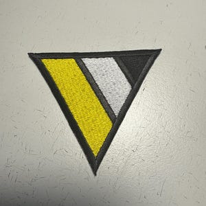 Könnte beinhalten: Gestickter Aufnäher in Dreiecksform. Der Aufnäher hat ein gelbes, weißes und schwarzes Design mit einem schwarzen Rand. Der gelbe Bereich befindet sich links, der weiße in der Mitte und der schwarze rechts. Der Aufnäher ist wahrscheinlich für Kleidung oder Accessoires.