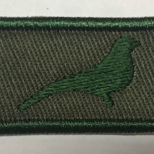 Puede incluir: Un parche bordado verde con una silueta de pájaro verde oscuro sobre un fondo verde claro.