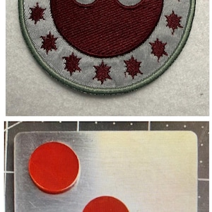 以下が含まれることがあります： グレーの背景に、マルーン色の反乱同盟軍のシンボルが刺繍されたパッチ。マルーン色のスターバーストで囲まれています。その下に、4つの赤い円形オブジェクトが付いた金属板があります。