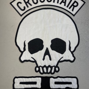 May include: White skull patch with black eyes, nose, and mouth. Above the skull is a black arched patch with the text "CROSSHAIR". Below the skull is a black rectangular patch with two white horizontal lines.