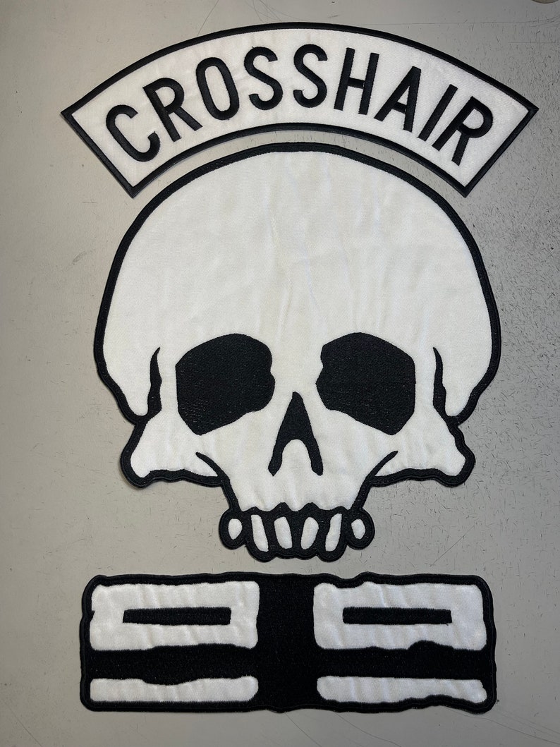 May include: White skull patch with black eyes, nose, and mouth. Above the skull is a black arched patch with the text "CROSSHAIR". Below the skull is a black rectangular patch with two white horizontal lines.