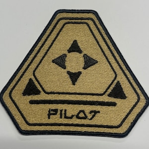 May include: A tan and black embroidered patch with a geometric design and the word "PILOT" in black lettering.