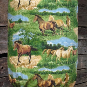 May include: A green, blue, and brown fabric cover with a repeating pattern of horses running through a field. The horses are brown, white, and black.