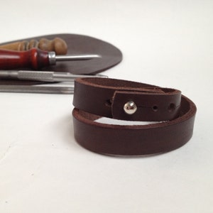 May include: A brown leather bracelet with a silver snap closure.