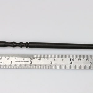 May include: A black wooden tool with a pointed tip and a textured handle. The tool is about 6 inches long and is measured against a ruler.