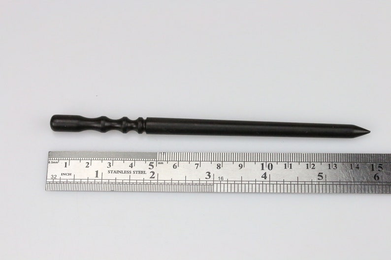 May include: A black wooden tool with a pointed tip and a textured handle. The tool is about 6 inches long and is measured against a ruler.