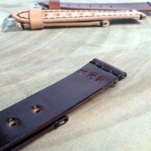 May include: A dark brown leather watch strap with black stitching and the word "MEP" embossed on the strap.
