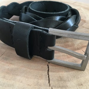 May include: A black leather braided belt with a silver buckle. The belt is coiled and the buckle is in focus.