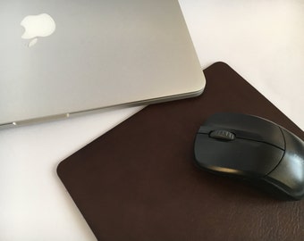 May include: A black wireless computer mouse on a brown leather mousepad. The mouse has a single button on the top and a scroll wheel.
