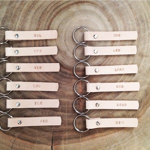 May include: Set of 10 leather keychains with silver key rings. Each keychain has a different acronym or abbreviation, including SOL, BFF, ILY, LOL, TLC, WTF, GR8, LBR, LMAO, OMG, XOXO, and BTW.