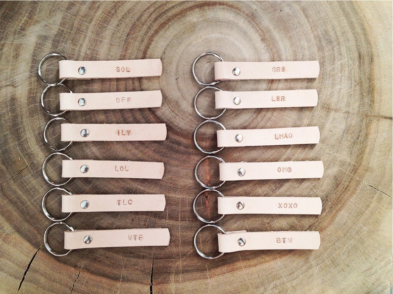 May include: Set of 10 leather keychains with silver key rings. Each keychain has a different acronym or abbreviation, including SOL, BFF, ILY, LOL, TLC, WTF, GR8, LBR, LMAO, OMG, XOXO, and BTW.