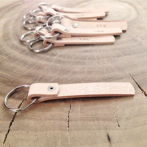May include: A set of six leather keychains with metal rings. Each keychain has a different word engraved on it, including "BFF" and "LOL".