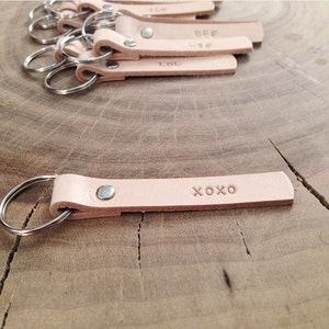 Könnte beinhalten: Ein Schlüsselanhänger aus hellbraunem Leder mit einem silbernen Ring und dem eingeprägten Wort "XOXO" auf dem Leder.
