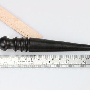 May include: A black wooden leather stitching tool with a rounded handle and a pointed tip. The tool is measured against a ruler that shows it is 6 inches long.