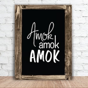 May include: A black chalkboard with a wooden frame, the words "Amok amok AMOK" are written in white on the chalkboard.