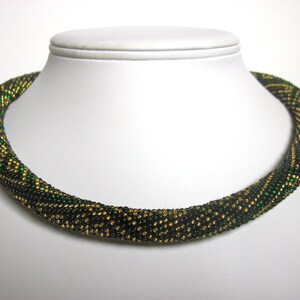 Op de afbeelding: Een groene en gouden kralenketting met een geometrisch patroon. De ketting is gemaakt van kleine, ronde kralen en is ongeveer 46 cm lang.