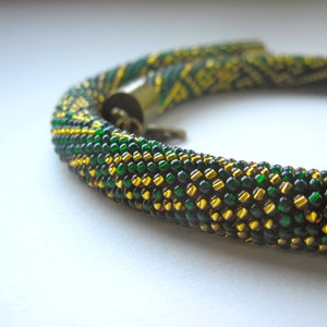 Op de afbeelding: Een groene en gouden kralenketting met een sluiting. De kralen zijn klein en cre&euml;ren een textuur.