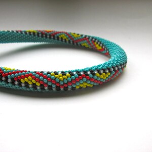 May include: Turquoise beaded bracelet with a colorful pattern. The bracelet features a repeating design of red, yellow, black, and white beads. The bracelet is made of small, round beads and has a clasp.