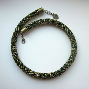 Op de afbeelding: Een groene en gouden kralenketting met een hartvormige sluiting.