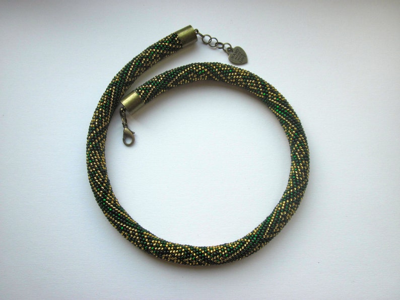 Op de afbeelding: Een groene en gouden kralenketting met een hartvormige sluiting.