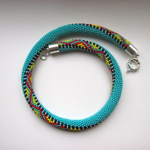 May include: Turquoise beaded necklace with a colorful geometric pattern. The necklace features a vibrant design with red, yellow, black, and white accents. It has a silver-tone clasp and is suitable for everyday wear.