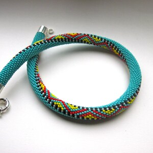 May include: Turquoise beaded necklace with a silver clasp. The necklace features a pattern of red, yellow, and black beads. The necklace is a choker style.