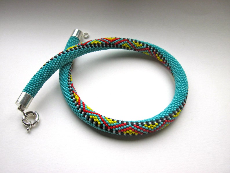 May include: Turquoise beaded necklace with a silver clasp. The necklace features a pattern of red, yellow, and black beads. The necklace is a choker style.