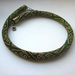 Op de afbeelding: Een groene en gouden kralenketting met een metalen sluiting.