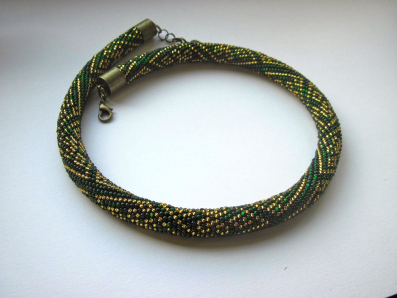 Op de afbeelding: Een groene en gouden kralenketting met een metalen sluiting.