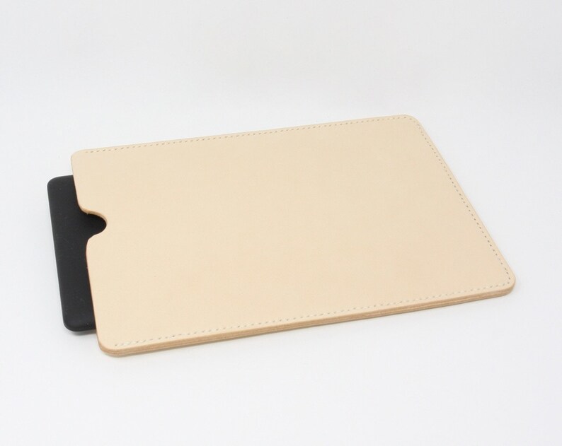 Puede incluir: Una funda de cuero beige claro con un rect&aacute;ngulo negro en el interior. La funda tiene un borde cosido.