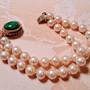 May include: A two-strand pearl bracelet with a gold clasp and a green oval stone set in a gold filigree setting. The pearls are a creamy white color and are evenly spaced.