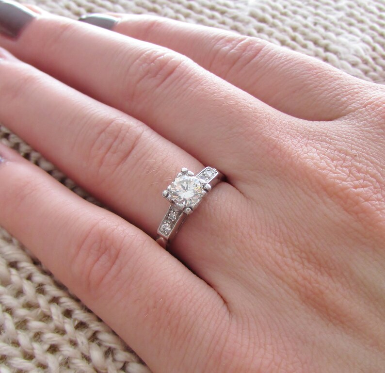 May include: A silver ring with a large, round, clear diamond in the center and smaller diamonds set in a band around the center stone.