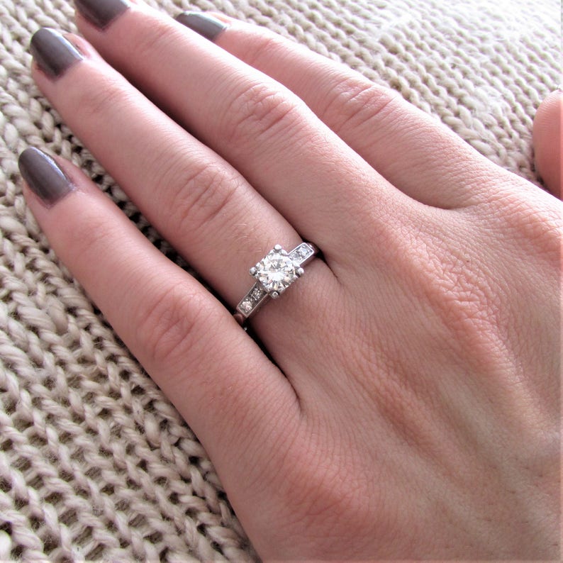 May include: A silver engagement ring with a round, clear center stone and smaller stones set in a band.