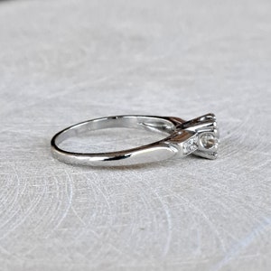May include: A silver engagement ring with a single round diamond and smaller accent diamonds on the band.