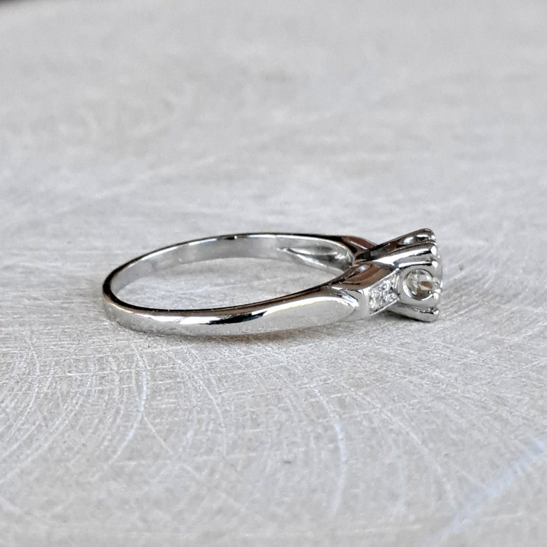 May include: A silver engagement ring with a single round diamond and smaller accent diamonds on the band.