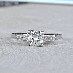 May include: A silver engagement ring with a single round diamond in the center and smaller diamonds set in a band.