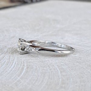 May include: A silver engagement ring with a round center stone and smaller accent stones on the band.