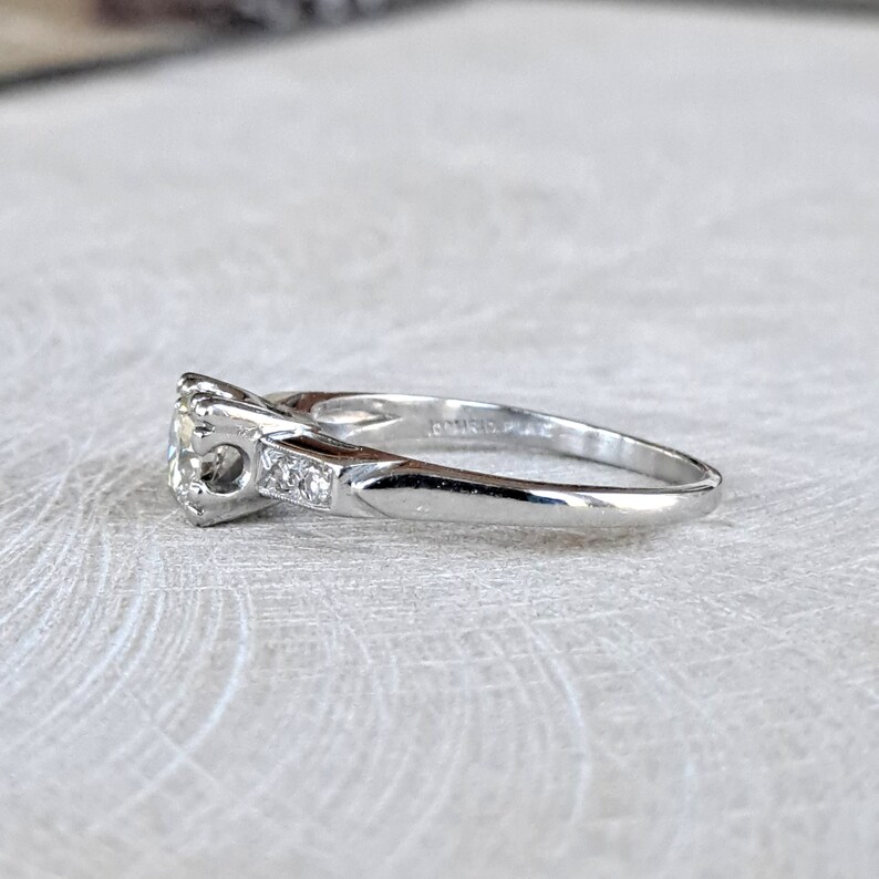 May include: A silver engagement ring with a round center stone and smaller accent stones on the band.