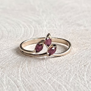 May include: A gold ring with three marquise-shaped pink gemstones set in a delicate, leaf-like design.