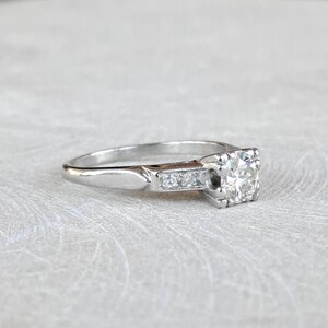 May include: A silver engagement ring with a round center diamond and smaller diamonds set in a band.