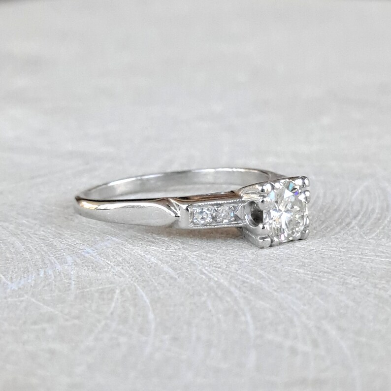 May include: A silver engagement ring with a round center diamond and smaller diamonds set in a band.