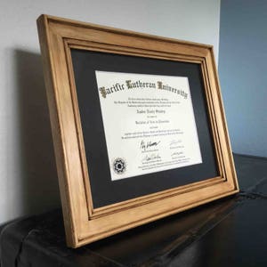 May include: A framed diploma from Pacific Lutheran University, awarded to Amber Nicole Stanley for a Bachelor of Arts in Education. The diploma is in a wooden frame with a black mat.